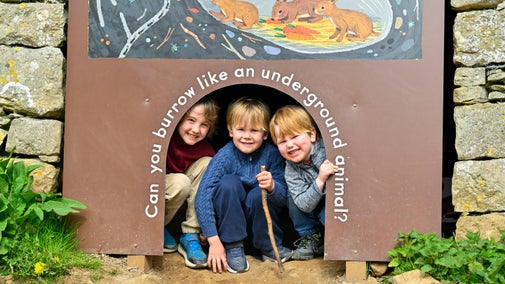 Children crouching inside a tunnel sign that reads “Can you burrow like an underground animal?”